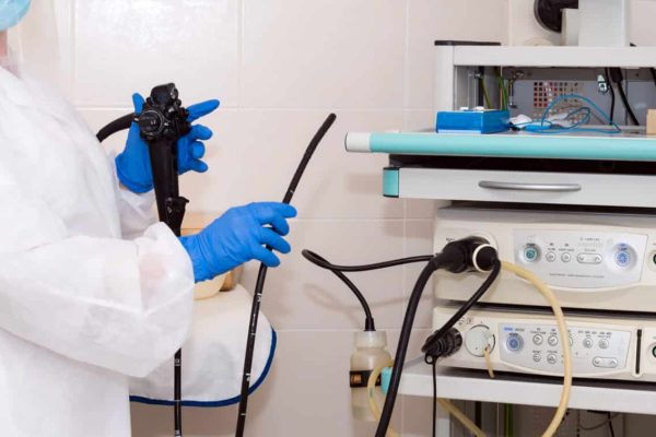 Doctor gastroenterologist in protective clothing holding endoscope before gastroscopy. Medical examination, medicine utensils and instruments, gastrointestinal fiberoptic endoscopy at modern hospital